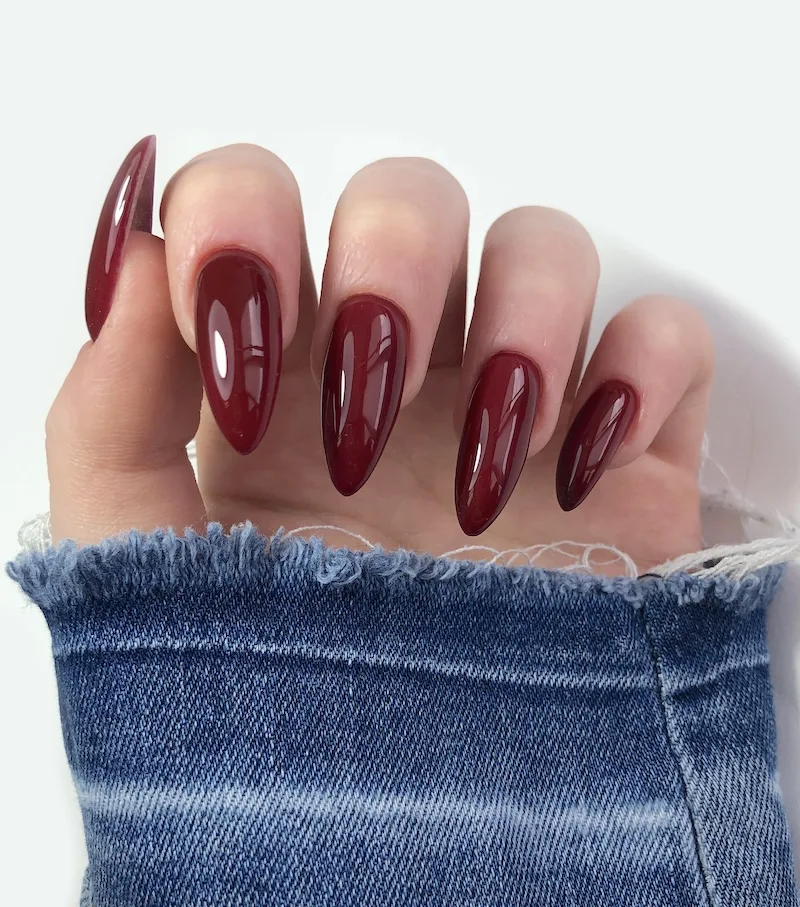 Deep red stiletto manicure on sleeve wearing demin jacket.