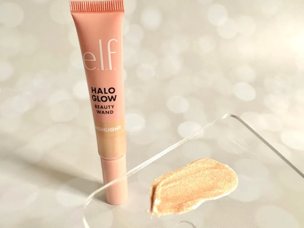 e.l.f. Halo Glow Highlight Beauty Wand in the shade Champagne Campaign next to highlighter sample on clear plastic spatula.