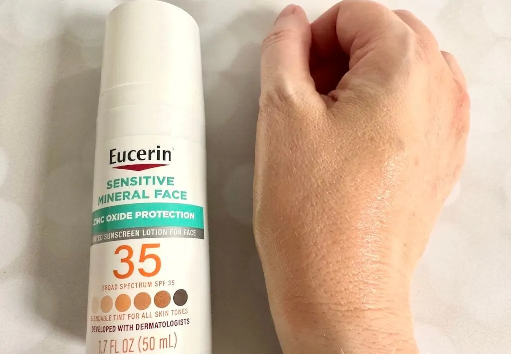 Eucerin Sensitive Tinted Mineral Face Lotion SPF 35, bottle flatlay next to sample absorbed on hand.