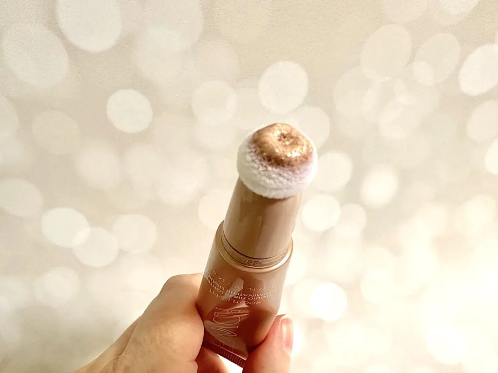 Flower Beauty Spotlight Liquid Highlight in the shade Opal next to highlighter sample on clear plastic spatula.