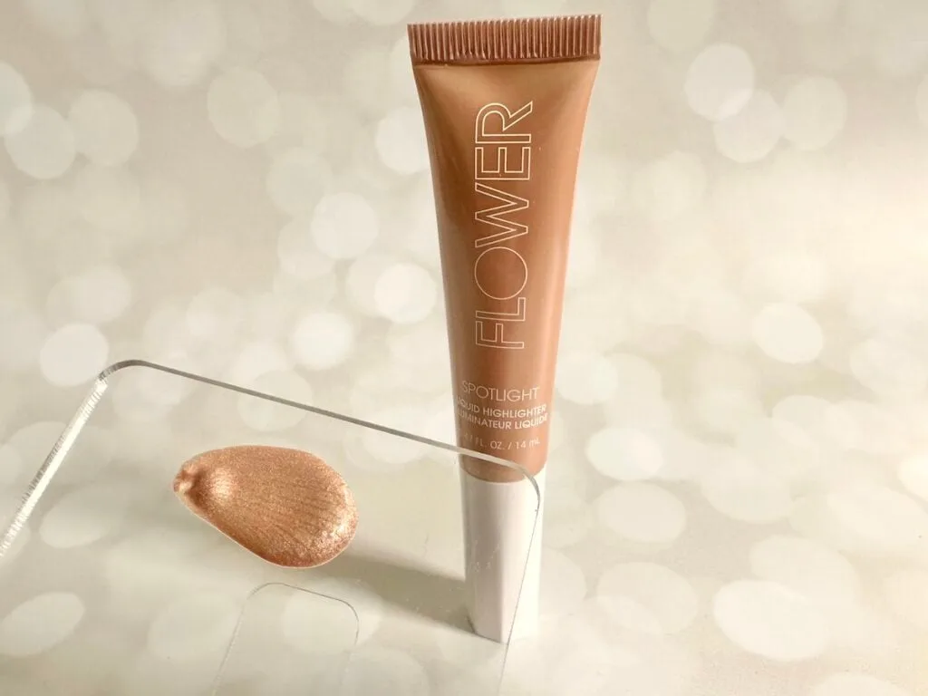 Flower Beauty Spotlight Liquid Highlight in the shade Opal next to highlighter sample on clear plastic spatula.