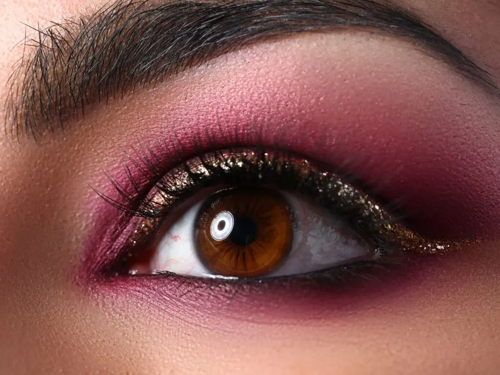 Matte burgundy eyeshadow with gold glitter at the lash line.