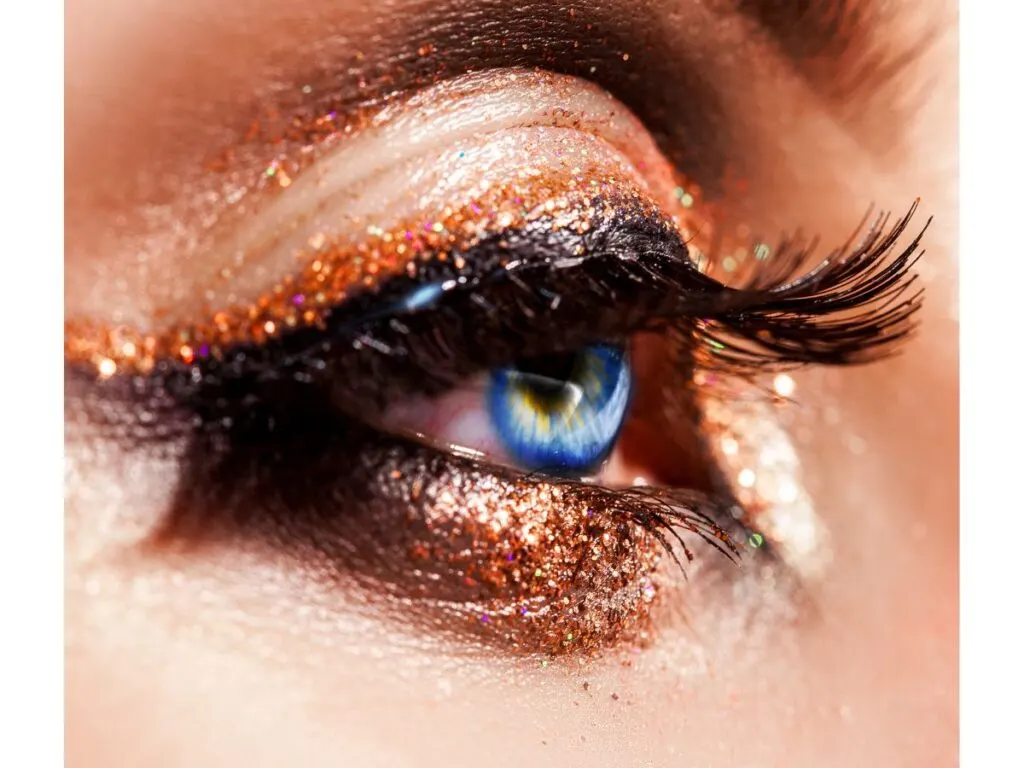 Side view of bronze glitter eyeshadow and liner on a bright blue eye.