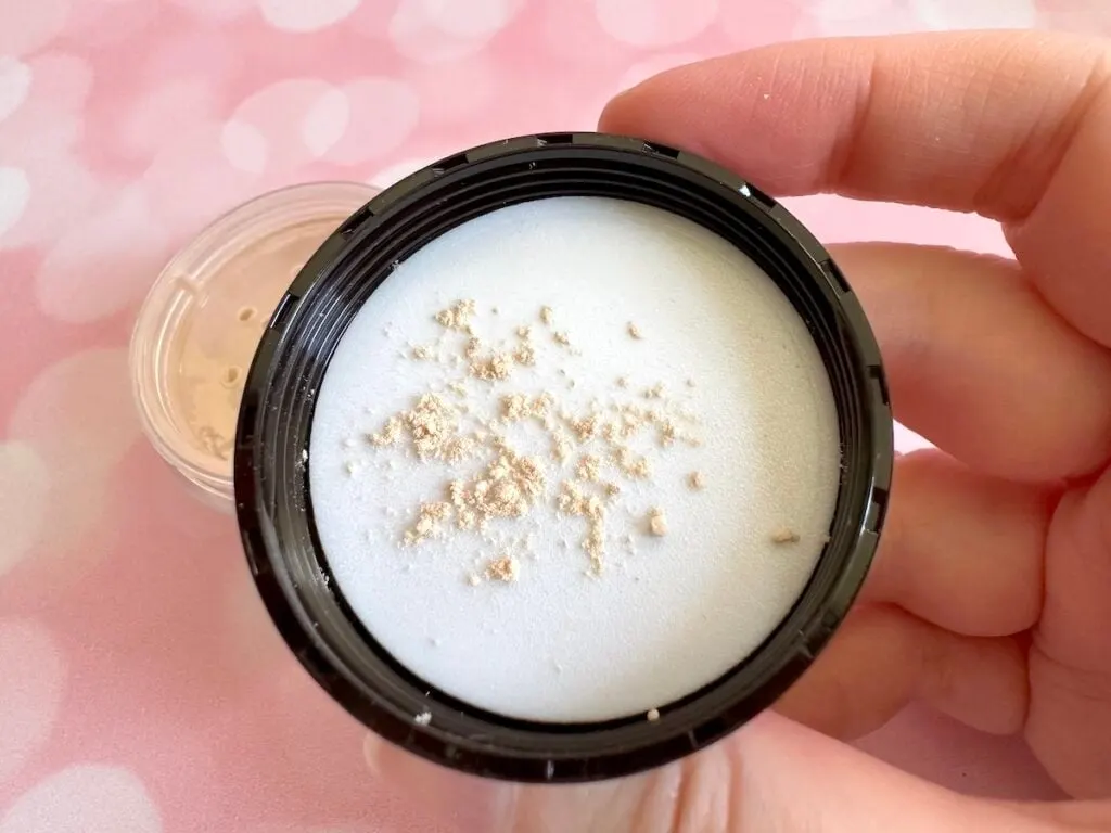 Laura Mercier Translucent Loose Setting Powder in the shade Translucent, open and sample in cap, handheld.