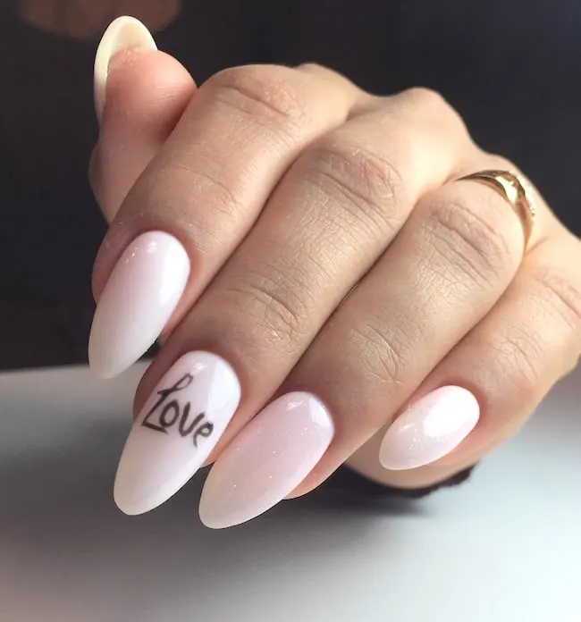 The word "love" inscribed on the middle nail of pink and white almond nails.