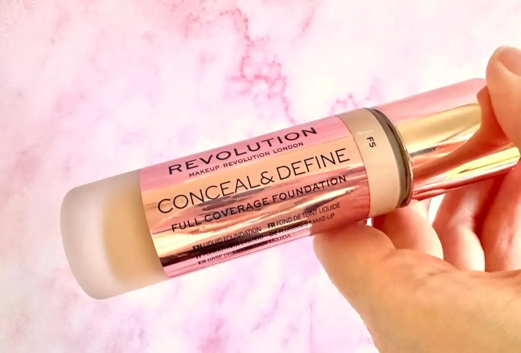 Makeup Revolution Conceal & Define Full Coverage Foundation in the shade F5, handheld.