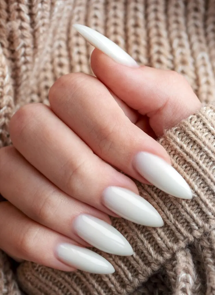 Milky white stiletto nails on beige knit sweater background.