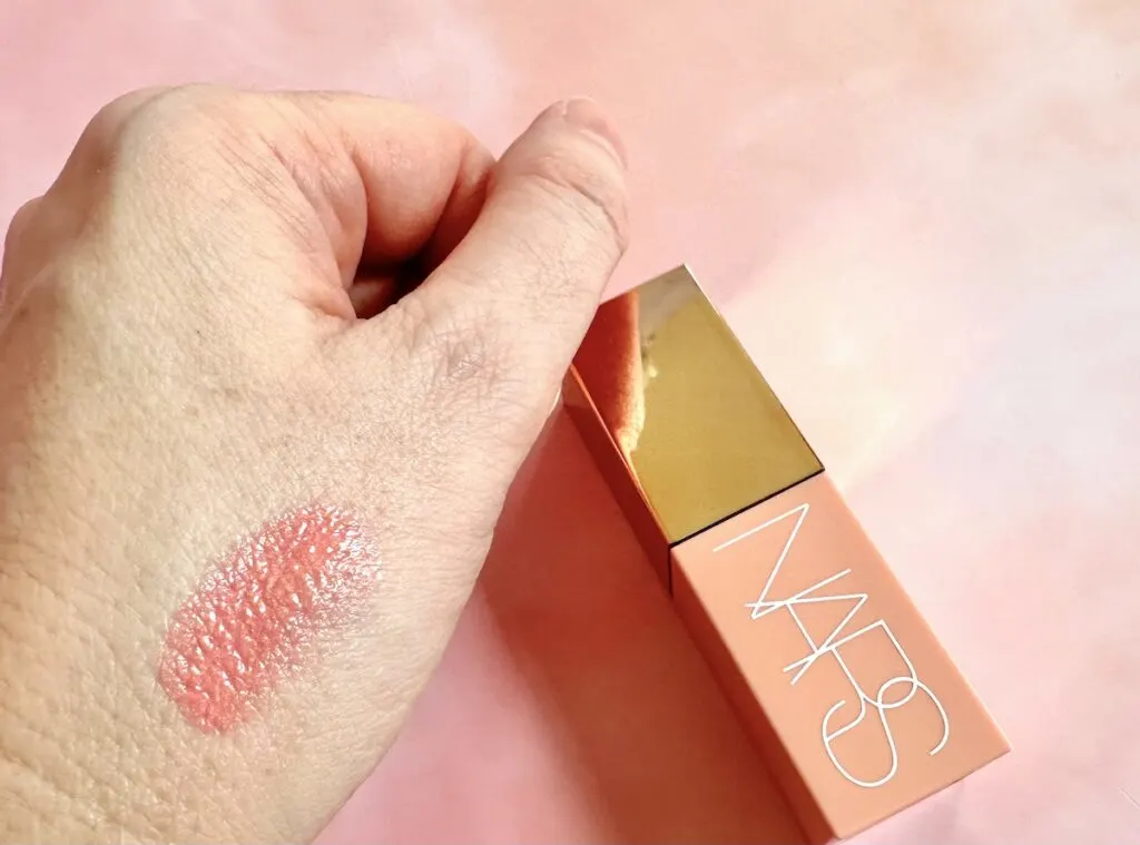 NARS Afterglow Liquid Blush in the shade Orgasm, flatlay next to sample on hand.