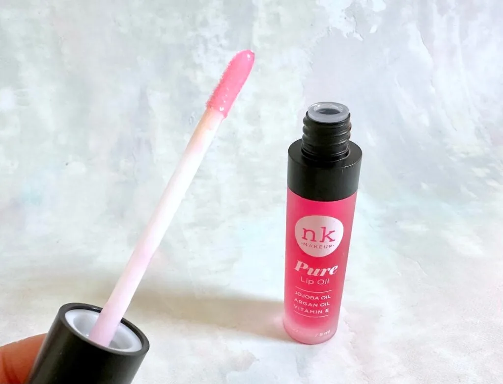 Nicka K Pure Lip Oil in the shade Raspberry, open tube with applicator wand, handheld.