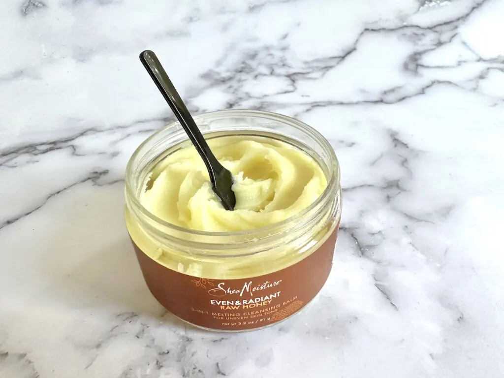 Shea Moisture Even & Radiant Raw Honey 3-in-1 Melting Cleansing Balm, open jar with black cosmetic spatula.