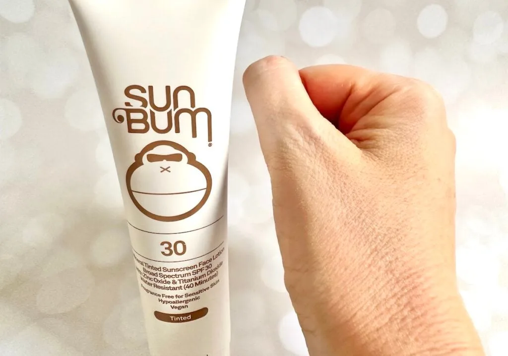 Sun Bum Mineral SPF 30 Tinted Sunscreen tube next to sample absorbed on hand.