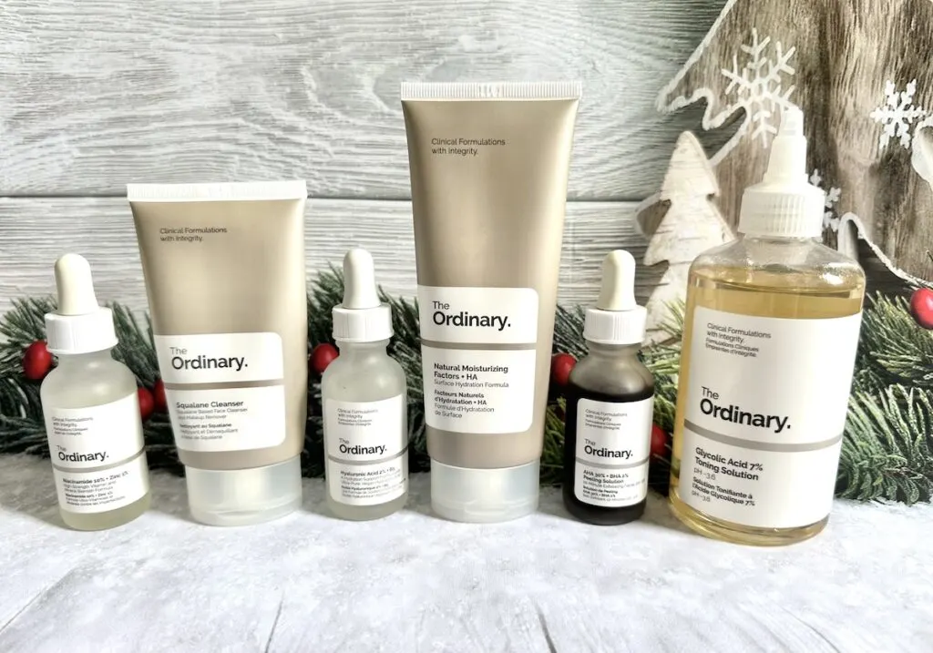 The Ordinary Black Friday Sale: The Ordinary Squalane Cleanser, The Ordinary Hyaluronic Acid, AHA 30% + BHA 1% Peeling Solution, The Ordinary Niacinamide Serum, The Ordinary Natural Moisturizing Factors + HA, and The Ordinary Glycolic Acid 7% Toning Solution in front of Christmas holly.