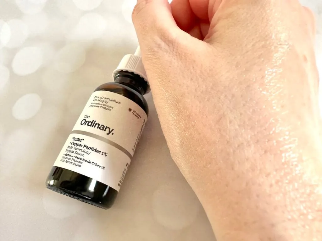 The Ordinary "Buffet" + Copper Peptides 1% Serum, bottle flatlay with sample absorbed on hand.