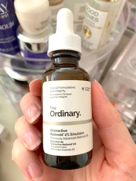 The Ordinary Granactive Retinoid 2% Emulsion, handheld in front of skincare products.