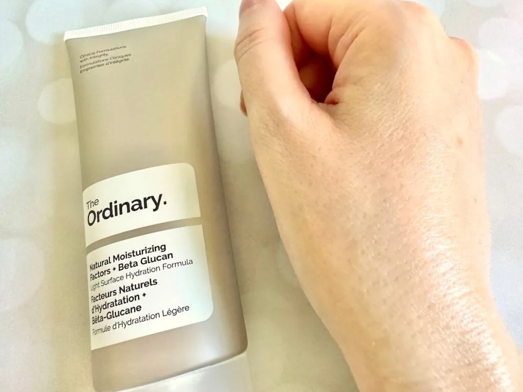 The Ordinary Natural Moisturizing Factors + Beta-Glucan, flatlay of tube next to sample absorbed on hand.