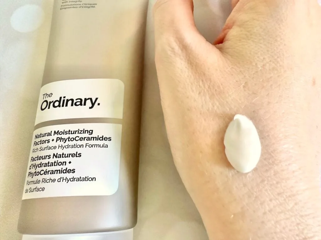 The Ordinary Natural Moisturizing Factors + PhytoCeramides, flatlay of tube, next to sample on hand.