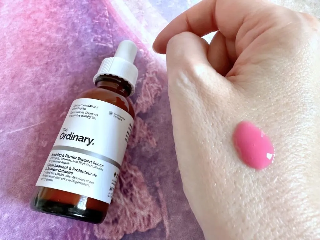 The Ordinary Soothing & Barrier Support Serum, flatlay of bottle next to a few drops of pink serum on hand.