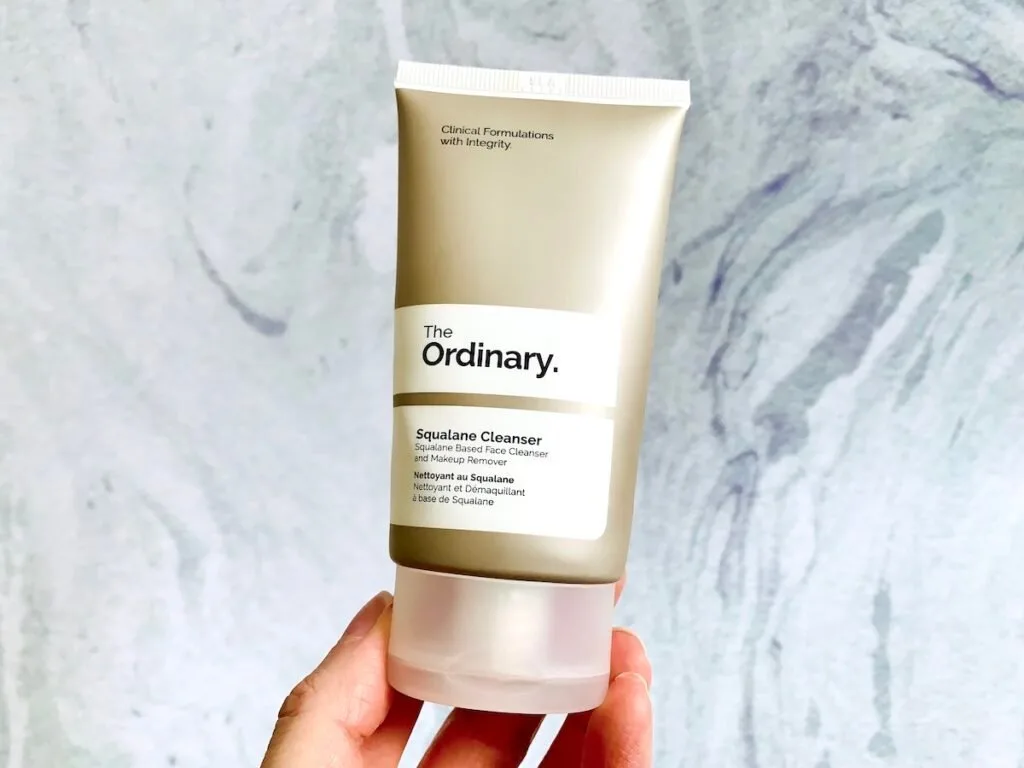 The Ordinary Squalane Cleanser handheld on a blue background.