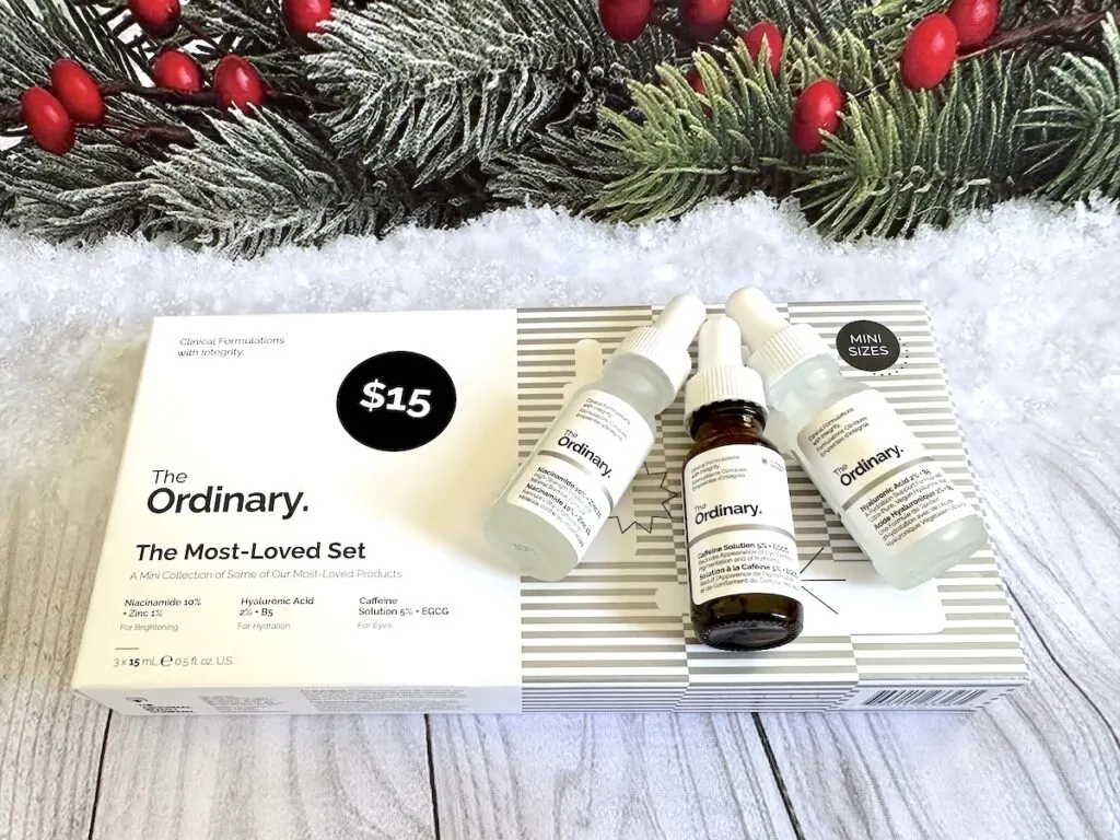 The Ordinary Most-Loved Best-Sellers flatlay with serum minis on top of box. Box in front of holiday garland.