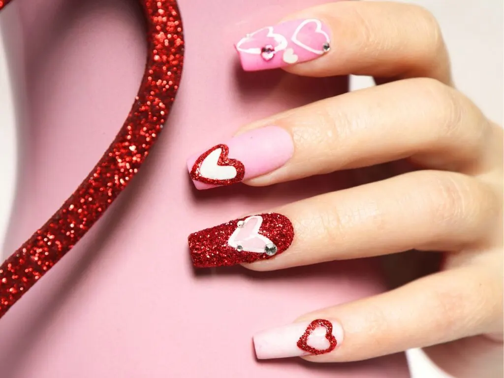 Maximal Valentine's Day-themed nail art with matte pink and glittery red textures on long nails. Half of a red glitttery heart on left.