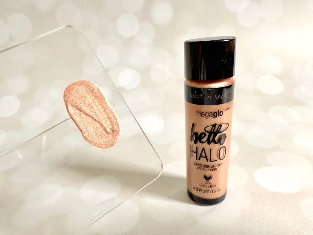 Wet n Wild MegaGlo Halo Liquid Highlighter in the shade Guilded Glow, next to highlighter sample on clear spatula.