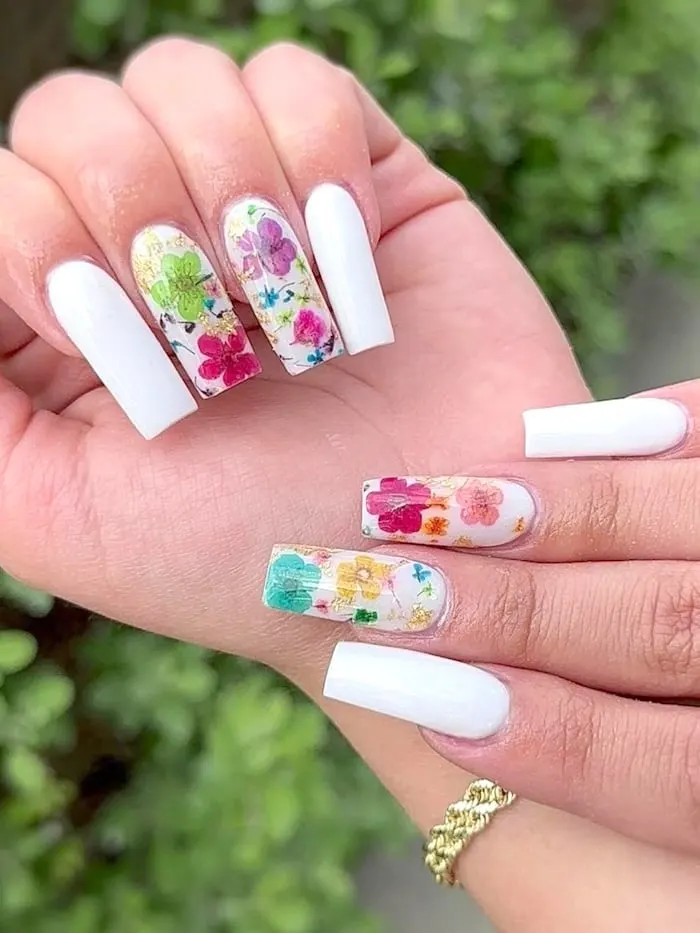 White nails with colorful flowers. Outside near greenery.