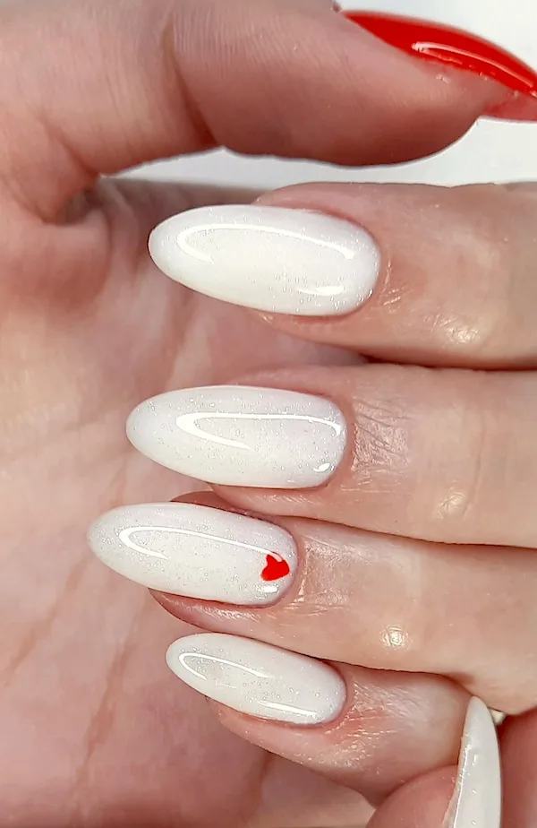 White almond nails with red heart on ring finger and red thumb nail.